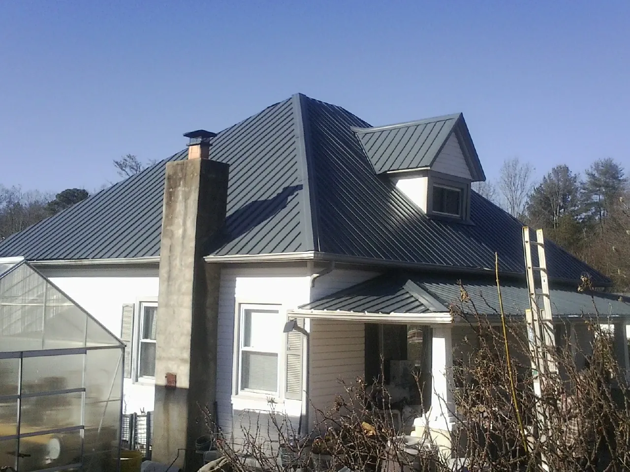 Dark blue standing seam metal roof on a white farmhouse with dormer — Slate & Tile Roof Repair by Roofing Brothers in Pleasanton