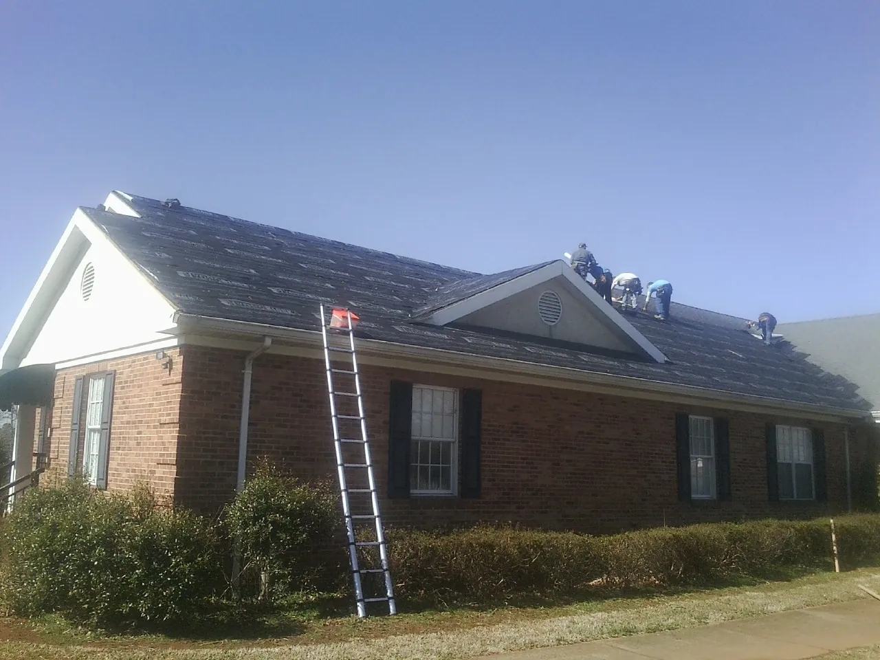 Crew tearing shingles off a brick ranch roof with a ladder set — Emergency Roof Repair work by our crew in Pleasanton