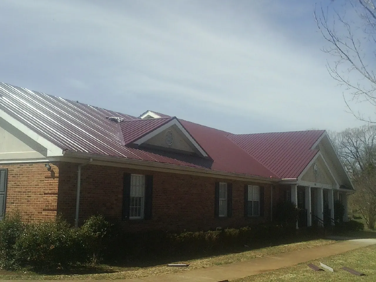 Red metal roof with gabled entries on a long brick building, from a Hail Damage Roof Repair job in Pleasanton