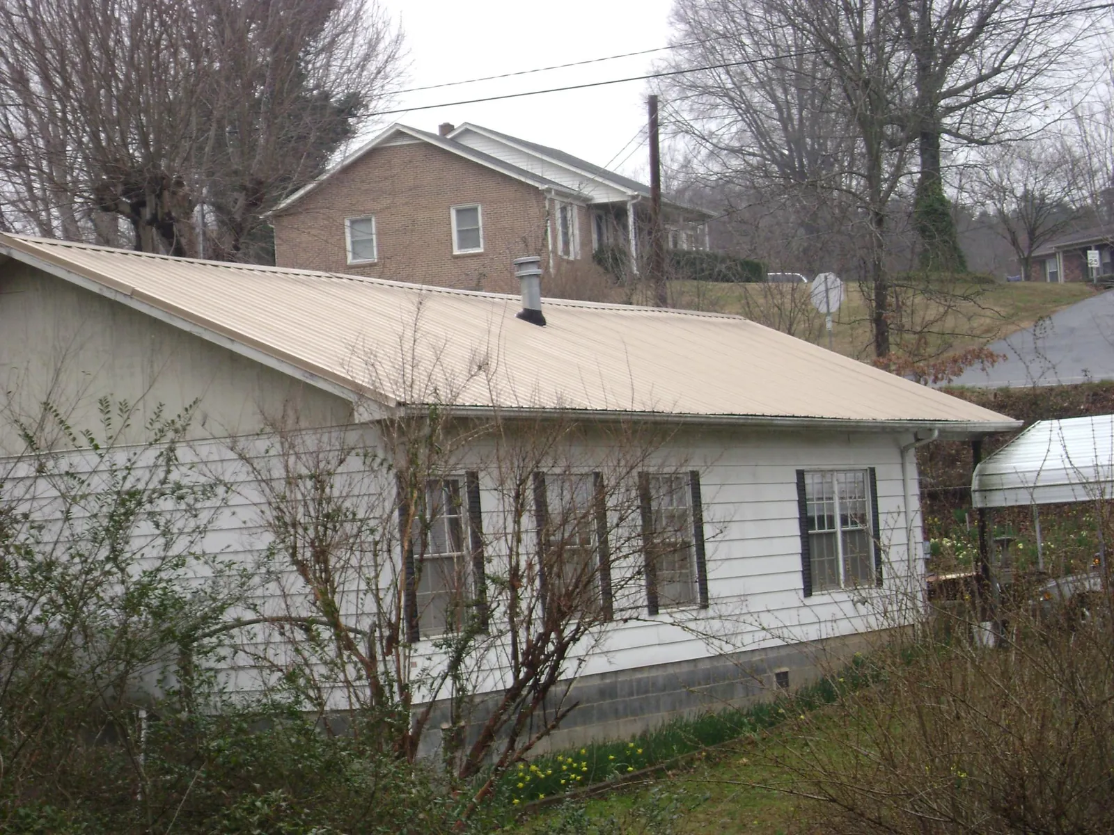 Tan metal roof on a white sided house set into a hillside — Commercial Roofing by Roofing Brothers in Pleasanton